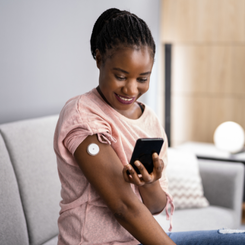 A woman looking at her phone while wearing a continuous glucose monitor.