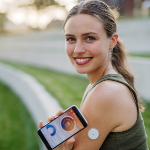 A woman smiling wearing a continuous glucose monitor.