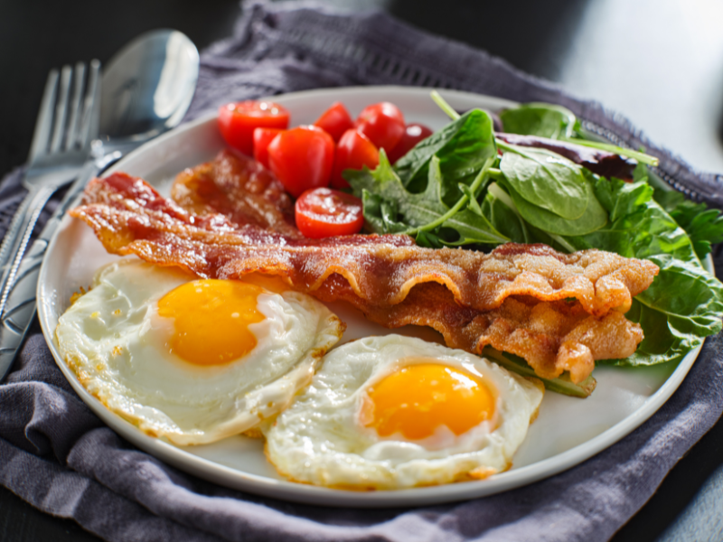 A plate of eggs, bacon, spinach, and tomatoes.
