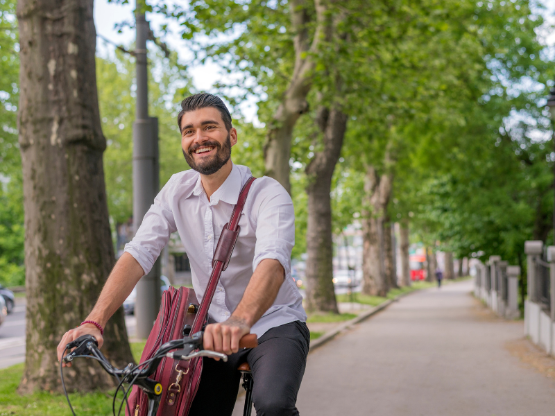 A smiling man riding a bicycle down a sidewalk.