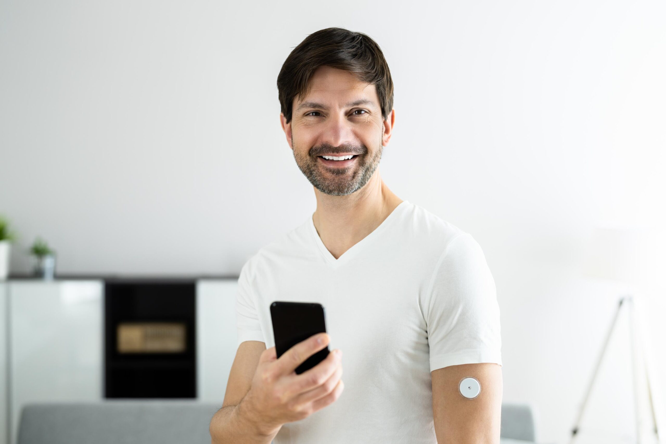 A man smiling wearing a continuous glucose monitor while holding his phone.