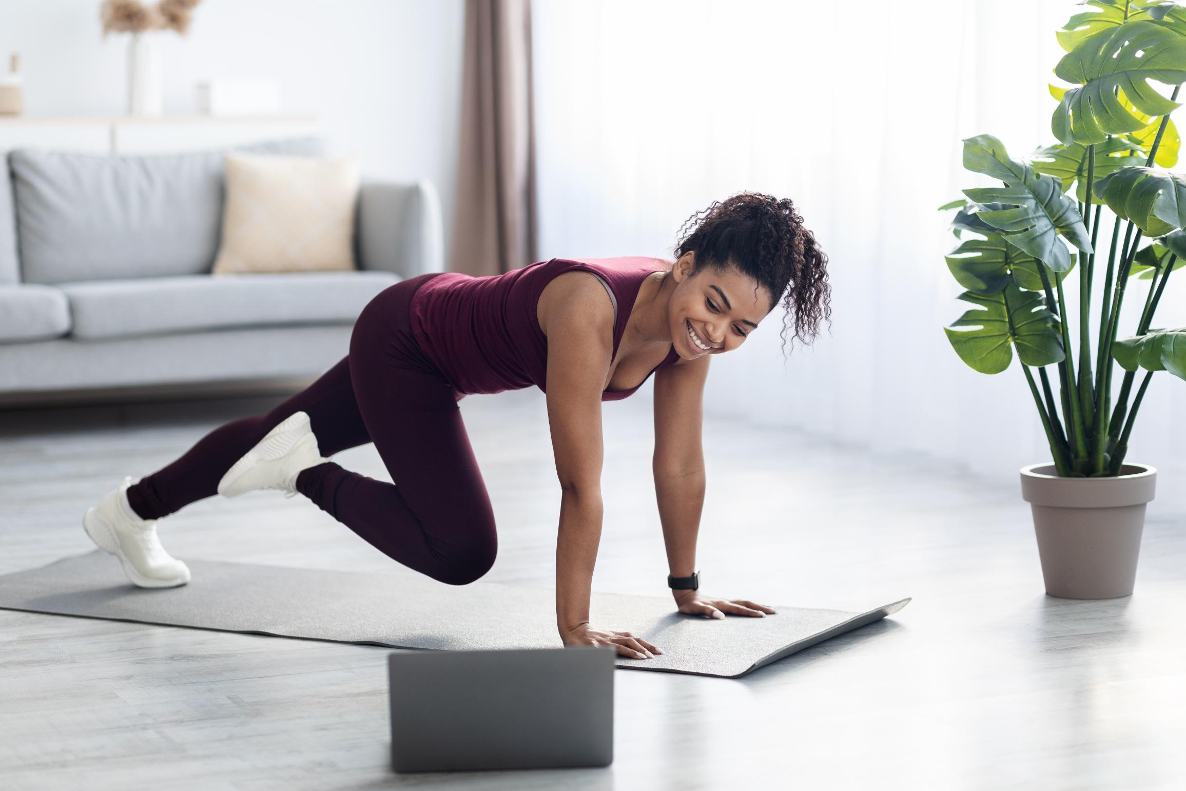 A woman exercising at home while following a workout on her laptop.