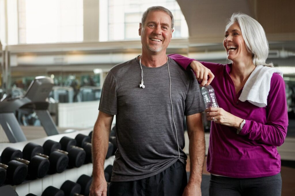 An older man and an older woman laughing together at the gym.